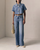 Person wearing a denim jacket and jeans holding a woven bag against a neutral background