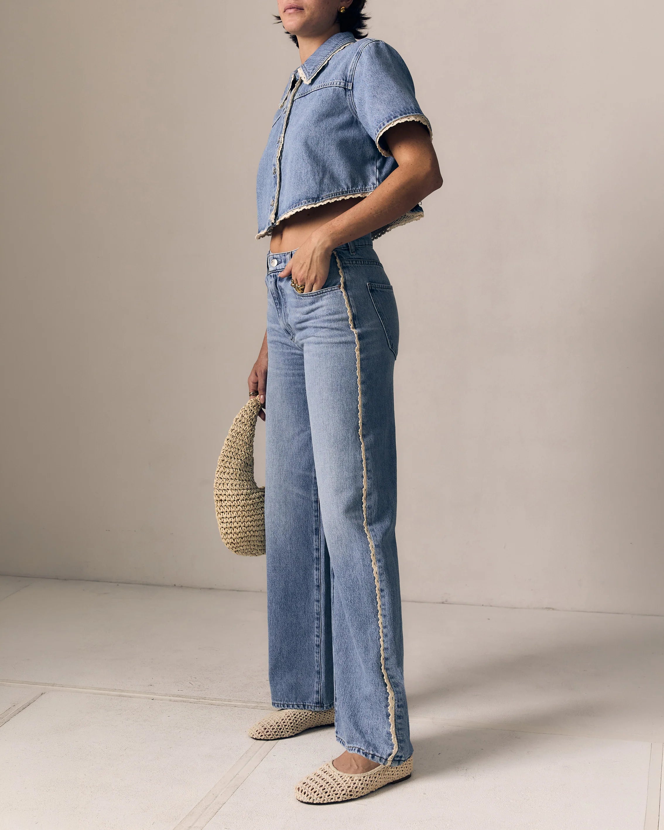 Person wearing a denim outfit with wide-leg jeans and a matching jacket against a neutral background.