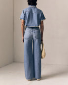 Person wearing a denim outfit with wide-leg jeans and a denim shirt, holding a woven bag.