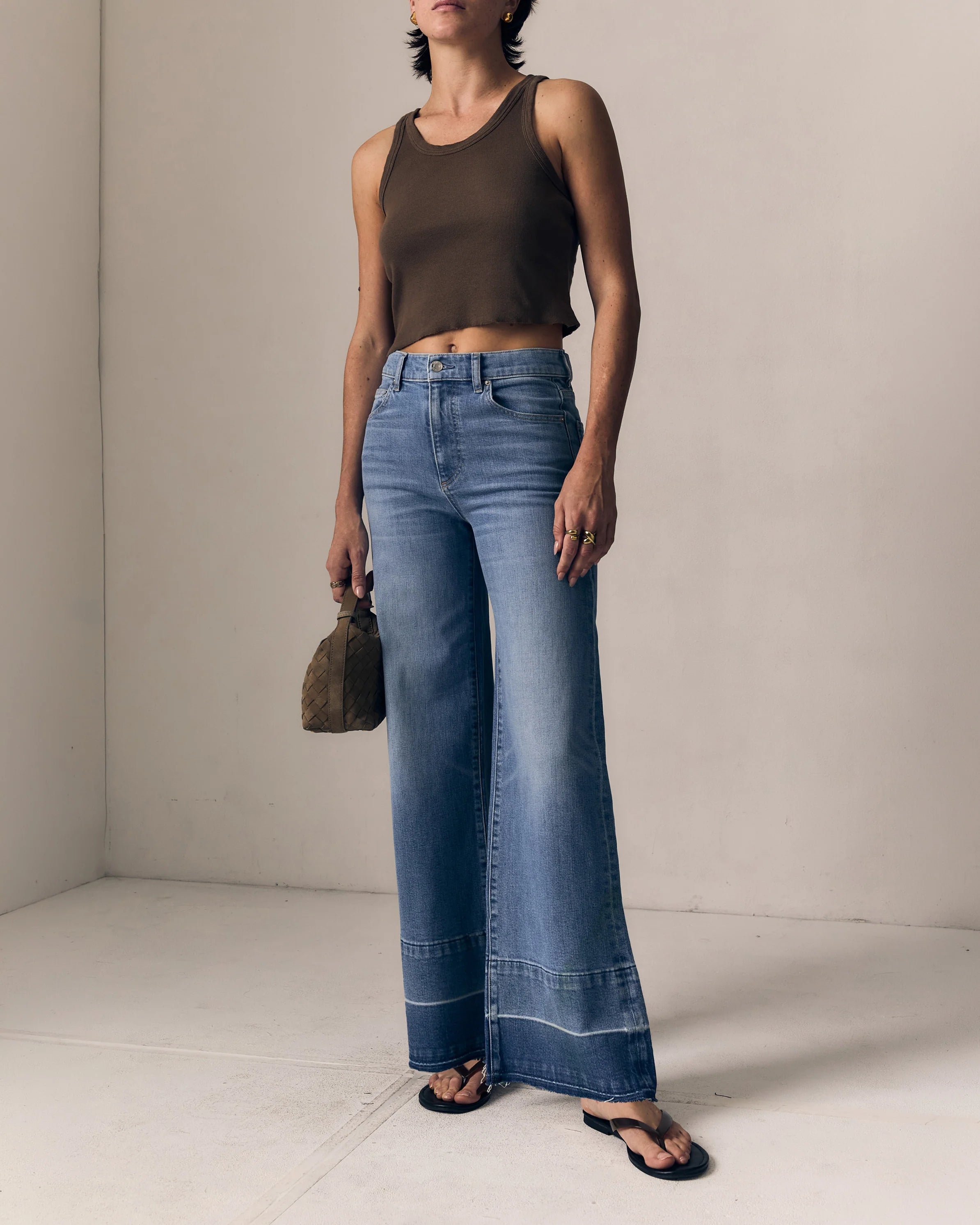 Woman wearing a brown top and blue jeans against a plain background