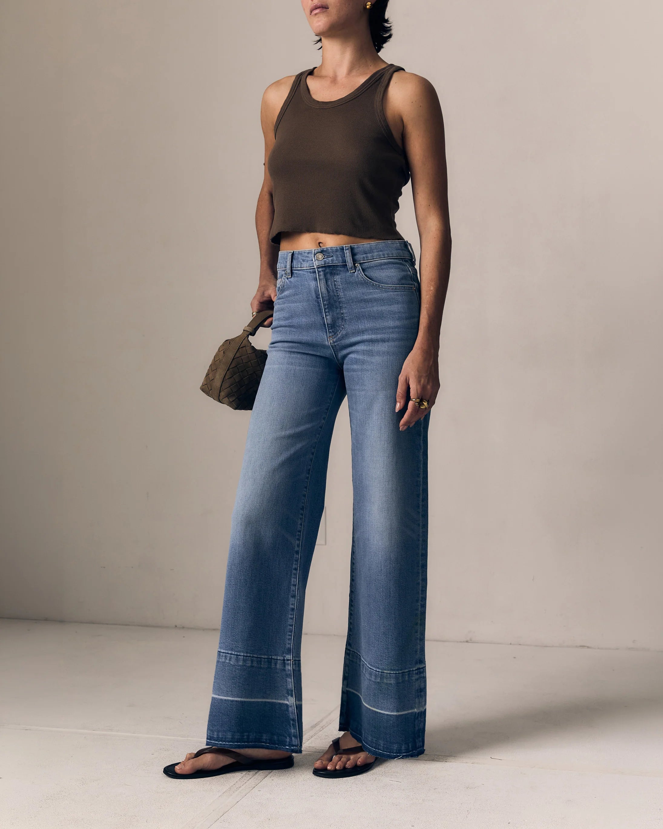 Person wearing a brown top and blue jeans against a neutral background