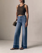 Person wearing a brown top and blue jeans against a neutral background