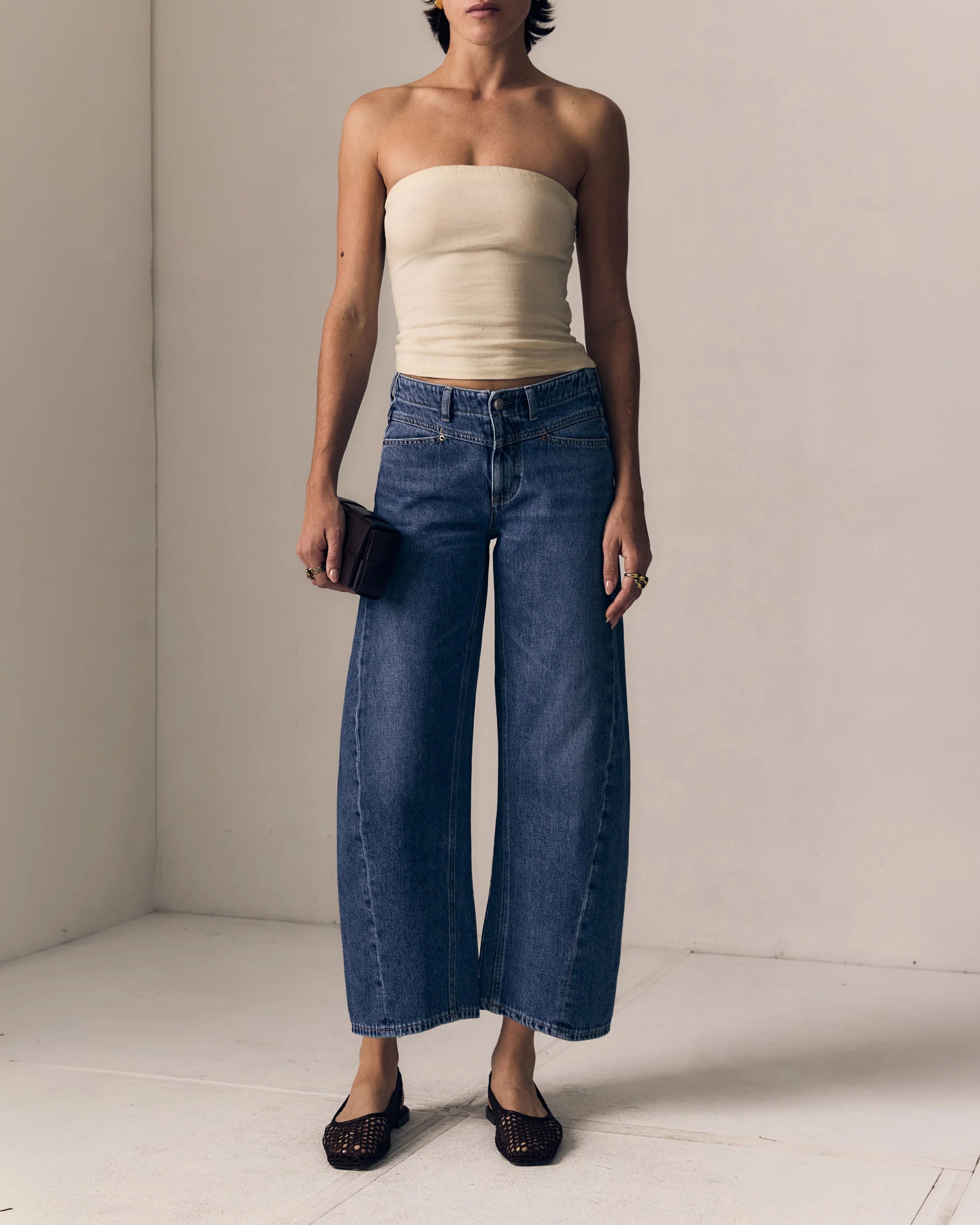 Woman wearing a strapless top and wide-leg jeans against a plain background