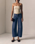 Woman wearing a strapless top and wide-leg jeans against a plain background