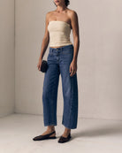 Woman wearing a strapless top and blue jeans against a plain background