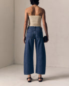 Woman wearing a strapless beige top and wide-leg blue jeans against a plain background