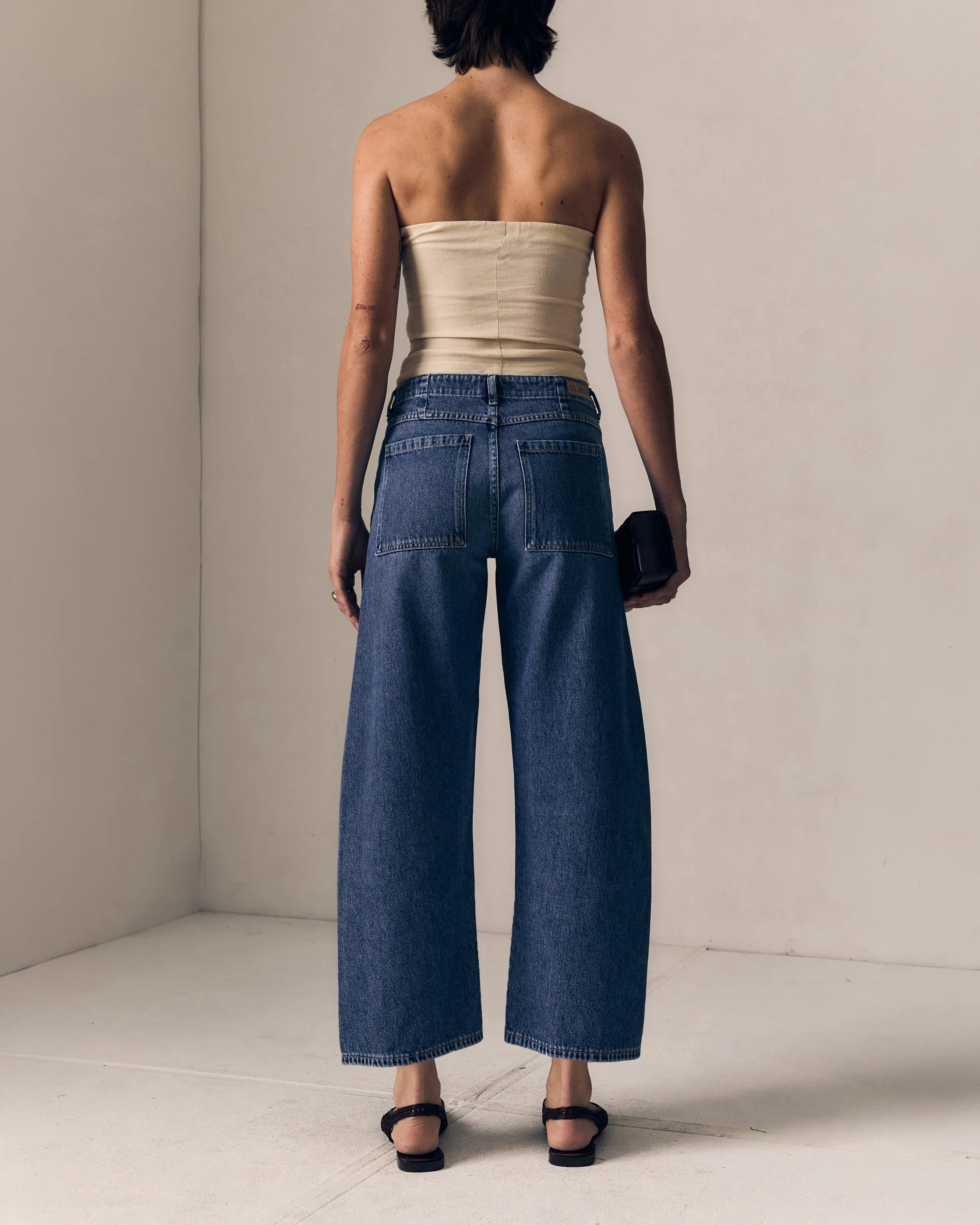 Woman wearing a strapless beige top and wide-leg blue jeans against a plain background