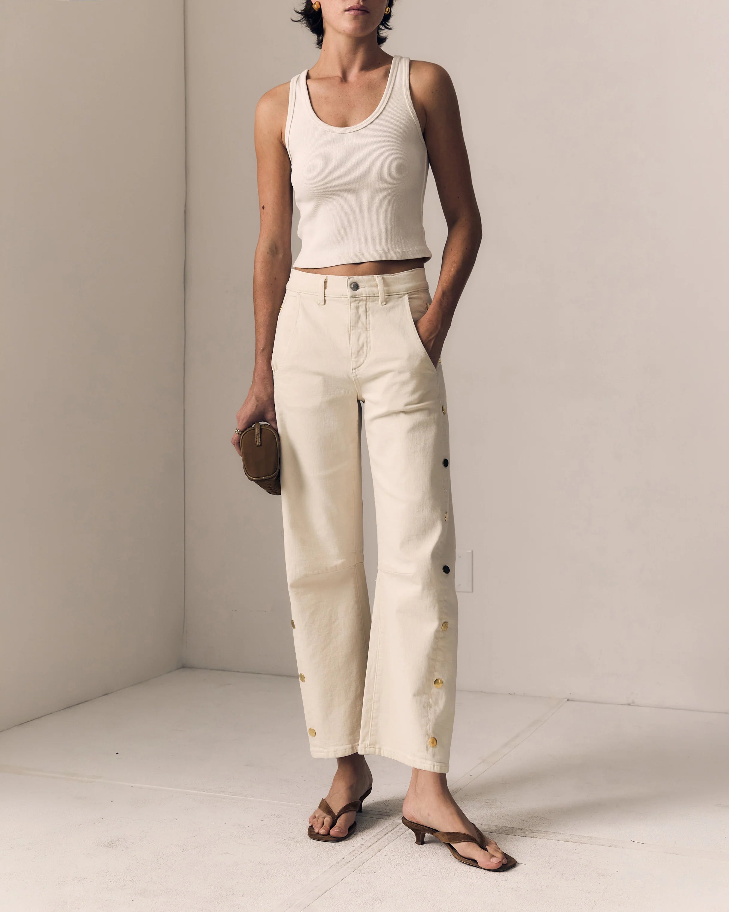 Person wearing a white tank top and beige pants in a minimalistic setting
