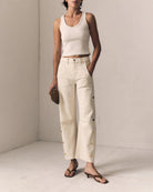 Person wearing a white tank top and beige pants in a minimalistic setting