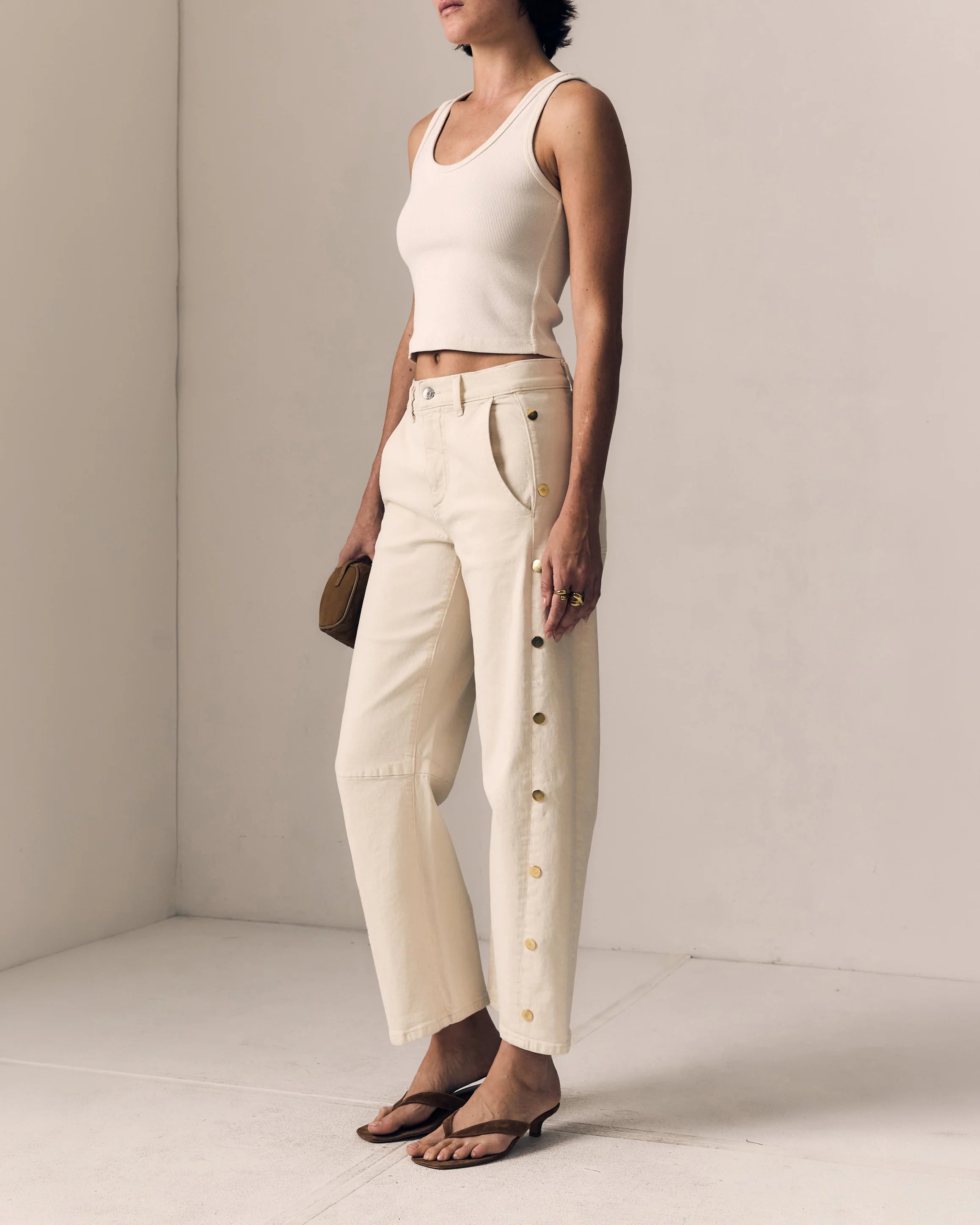 Woman wearing a white sleeveless top and beige pants against a plain background