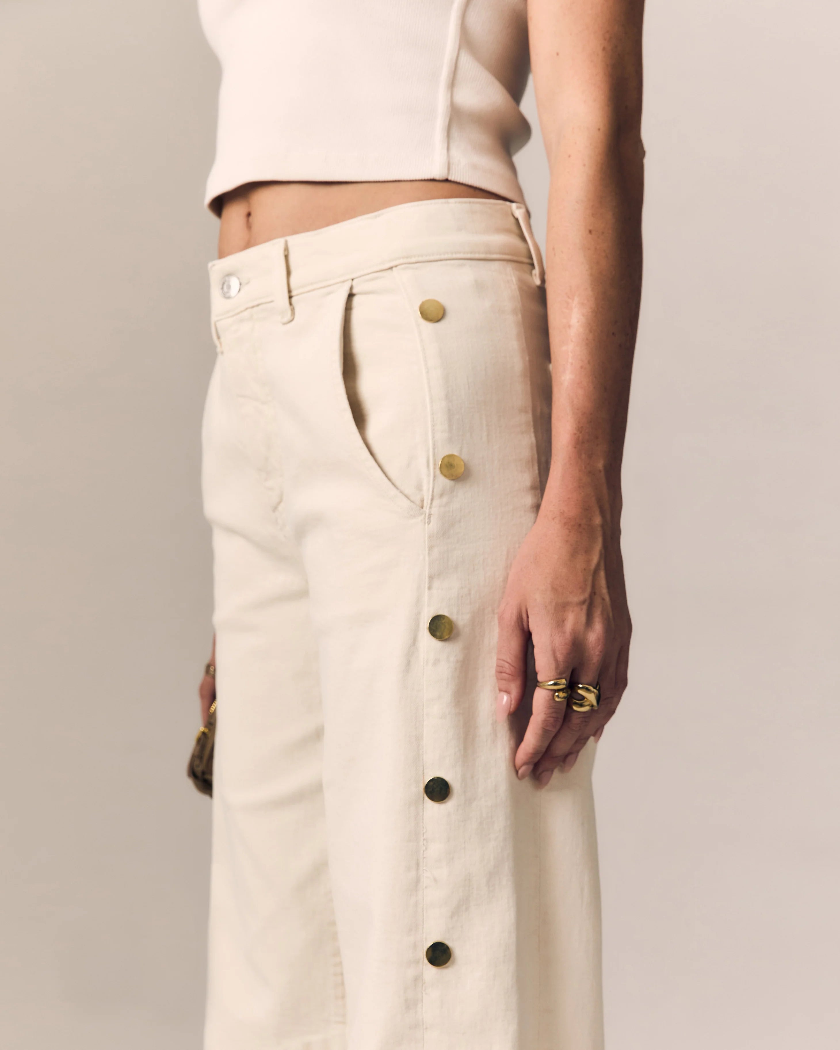 Person wearing beige pants with gold buttons against a neutral background
