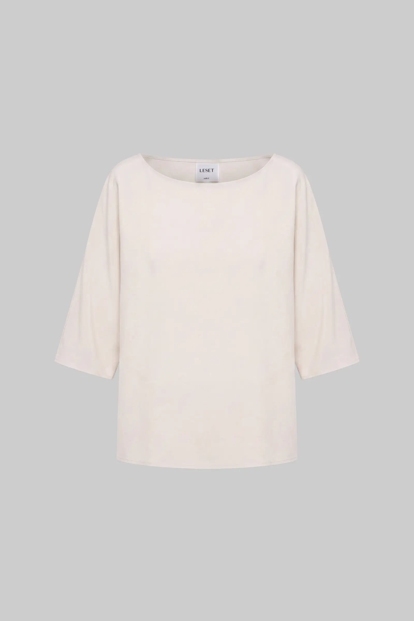 An off-white three-quarter sleeve top with a wide boat neckline, displayed against a solid gray background.