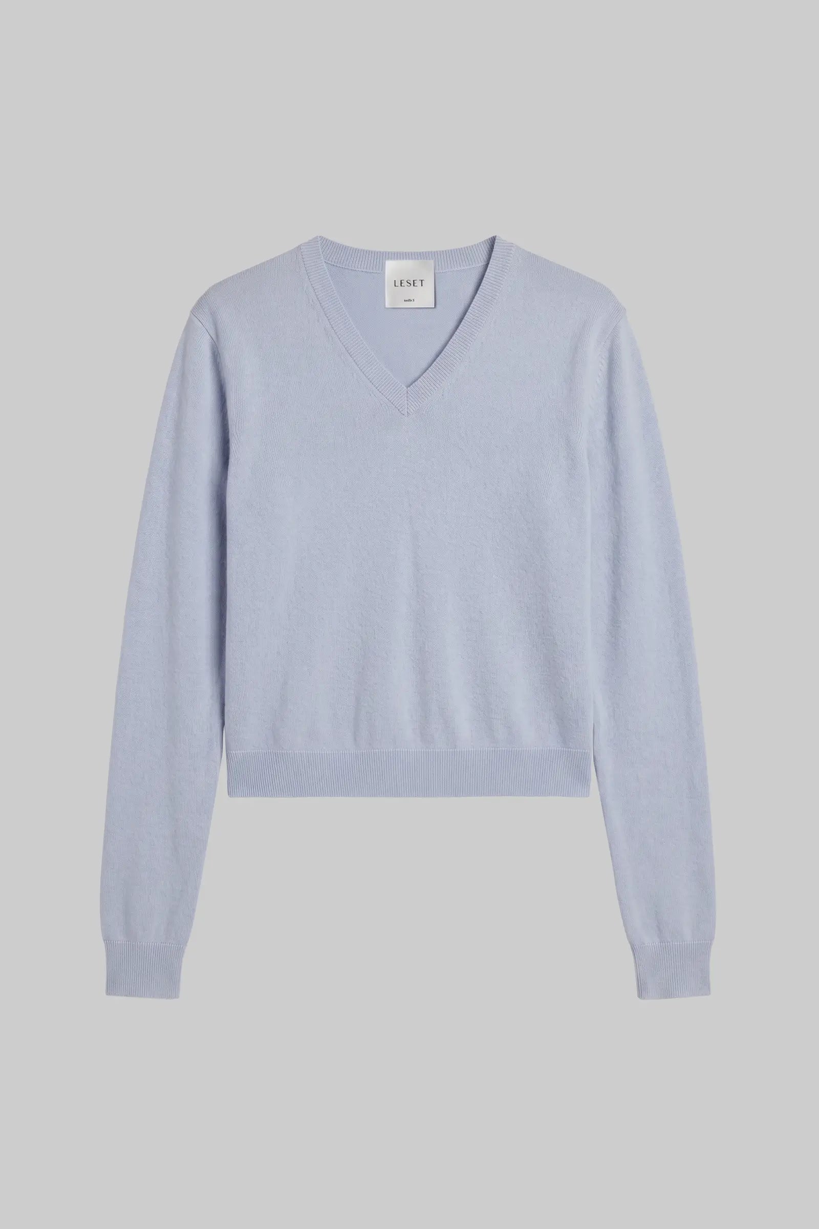 A light blue-gray V-neck knit sweater with long sleeves and ribbed cuffs and hem, displayed flat against a solid gray background.