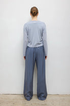 A woman modeling a light blue-gray long-sleeve cropped sweater with a bright turquoise inner collar and hem detail, paired with slate blue wide-leg trousers, against a plain light gray background from a back side view.
