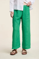 Person wearing green pants and a white shirt on a beige background