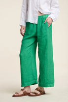 Person wearing green pants and a white shirt on a beige background