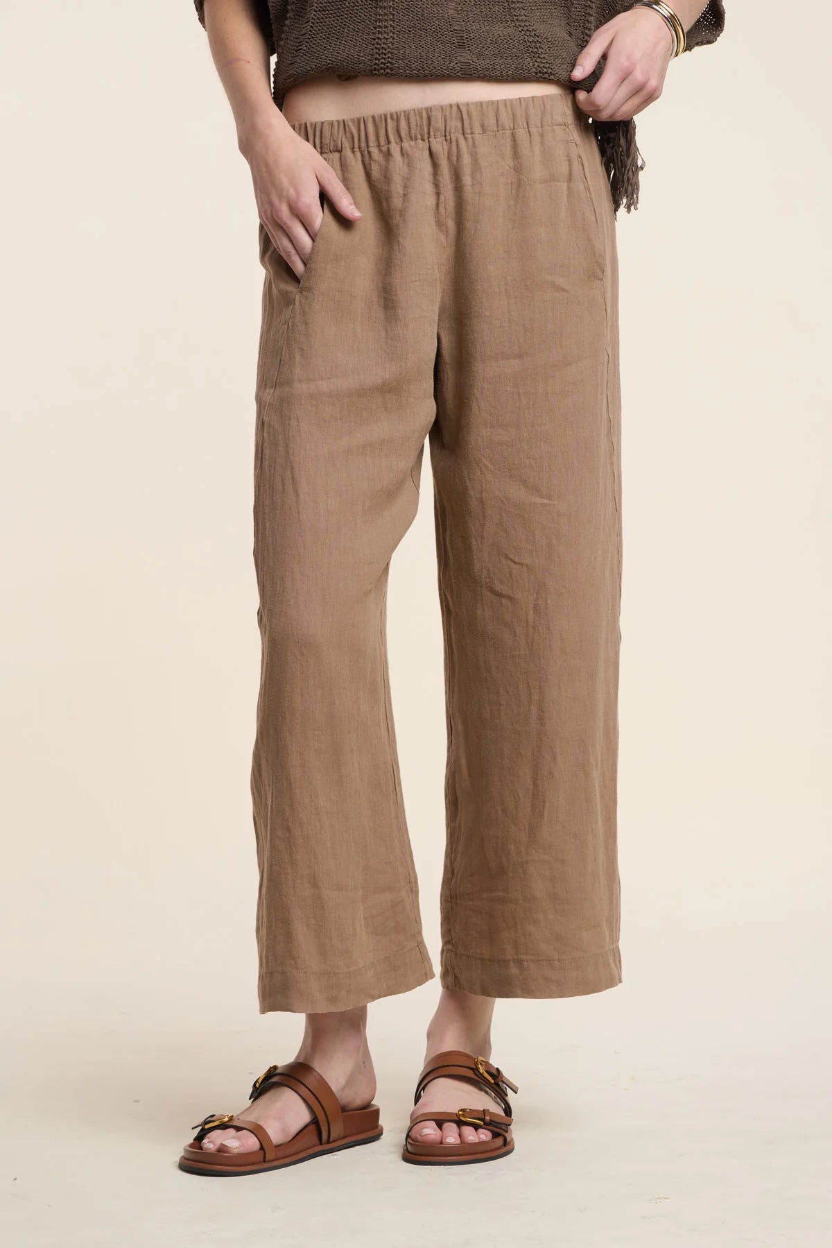 Person wearing brown linen pants on a beige background
