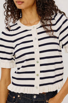 A close-up of a woman wearing a short-sleeve knit top with horizontal navy and off-white stripes, a round neckline, and a button-front closure with ruffled trim at the sleeves and hem.