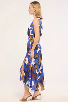 A woman modeling a sleeveless midi dress with a blue, brown, and white abstract pattern, shown from a side profile against a plain light background.