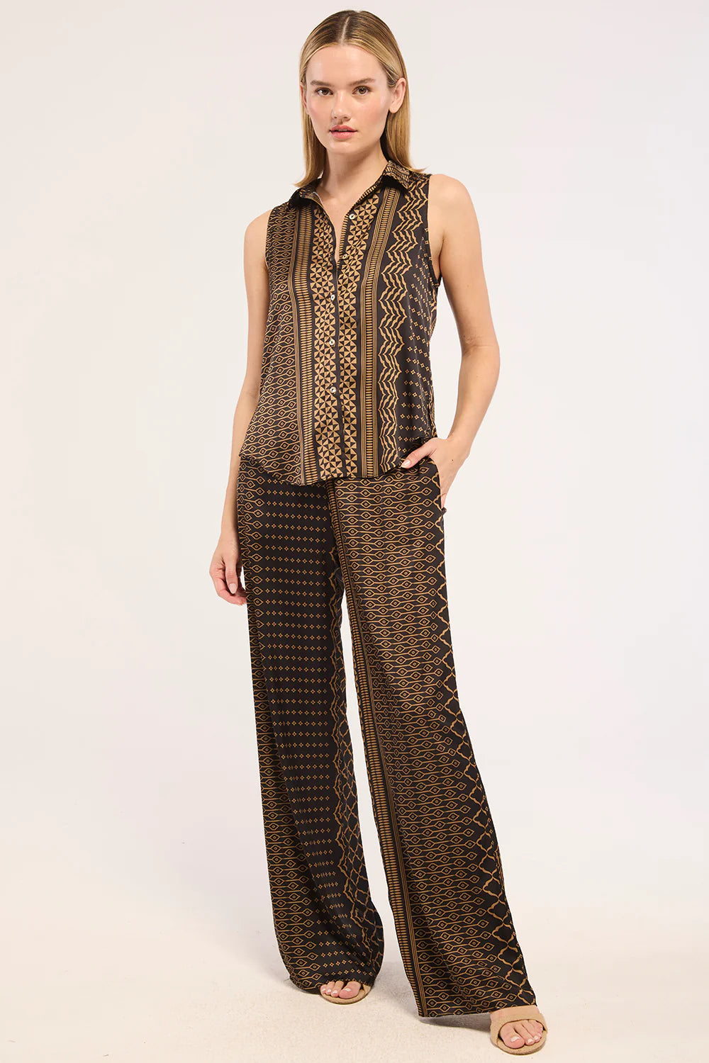 A woman modeling a matching sleeveless button-front top and wide-leg pants set in a brown and beige geometric pattern, photographed against a plain light background.