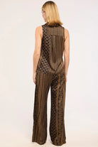 A woman viewed from the back wearing a sleeveless brown and black patterned jumpsuit with wide legs, photographed against a plain light background.