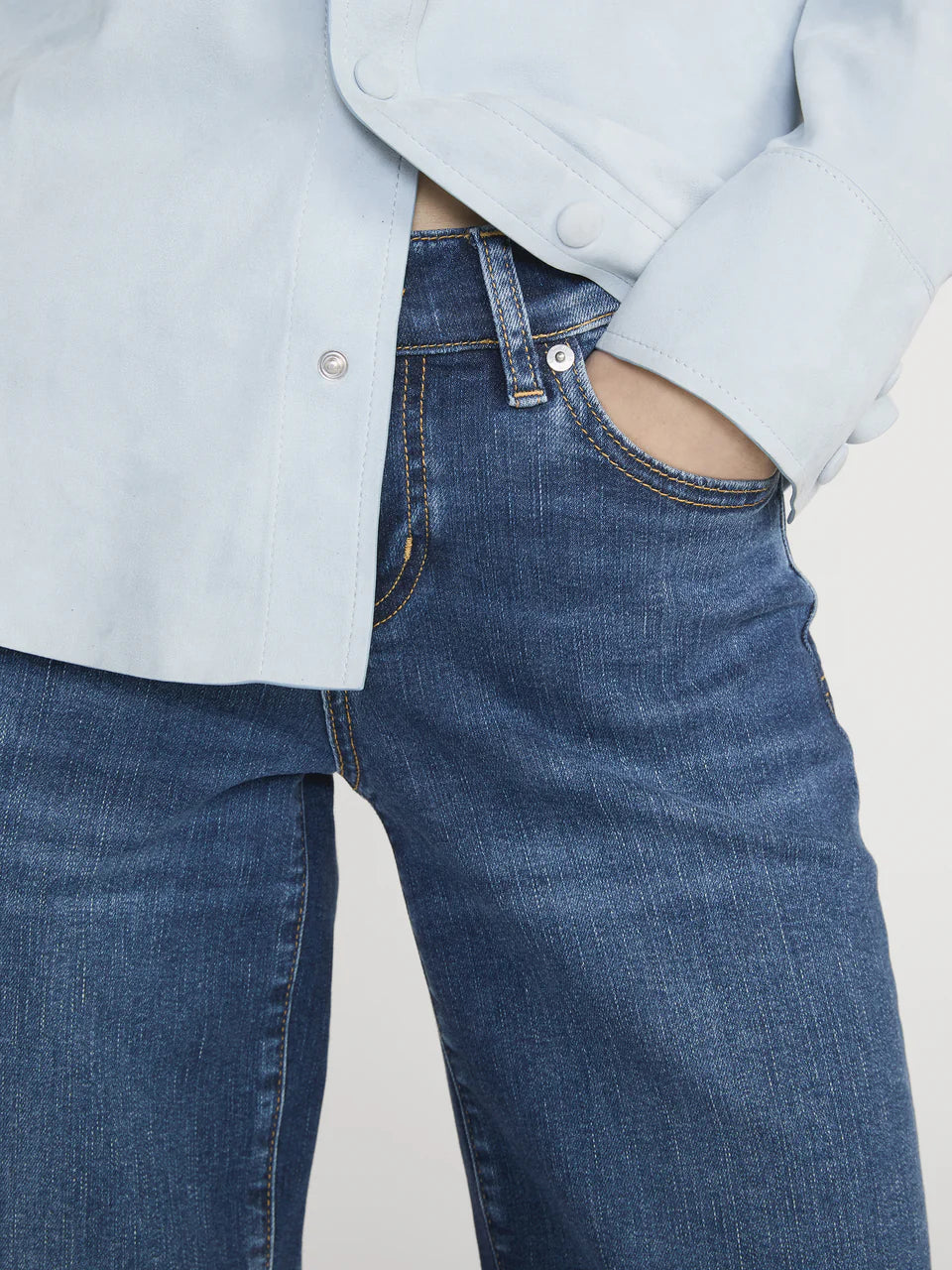 Person wearing blue jeans and a light blue jacket on a plain background