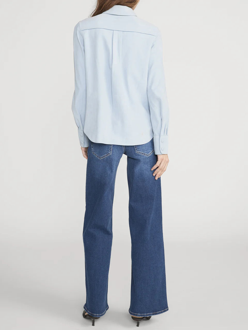 Person wearing a light blue shirt and blue jeans on a white background
