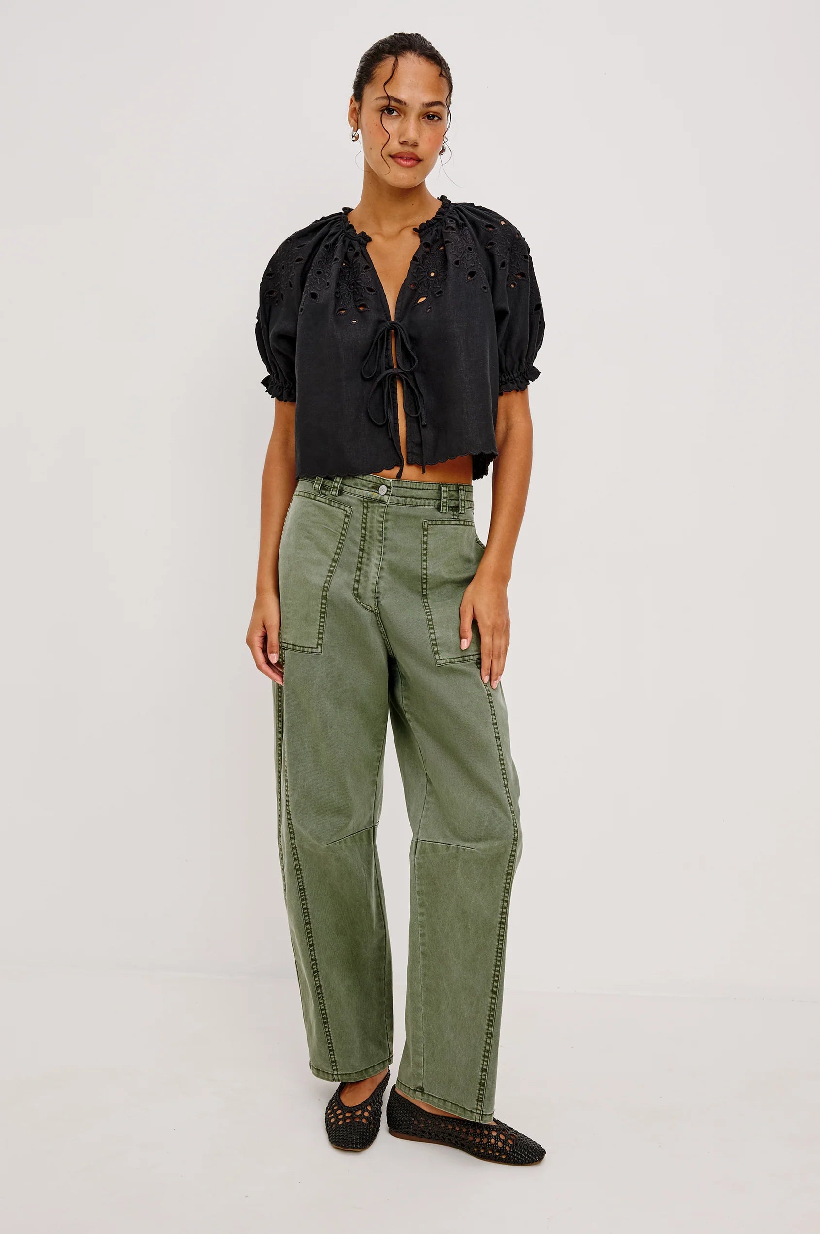 Woman wearing a black blouse and green pants on a white background