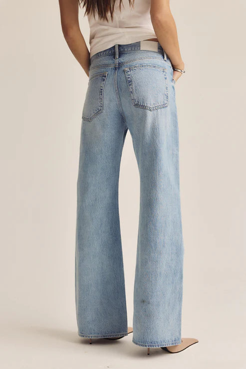 Person wearing light blue flared jeans on a beige background