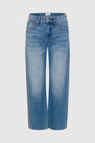 Light blue denim jeans with decorative gold-tone metal studs running down the front of each leg, shown against a light gray background.