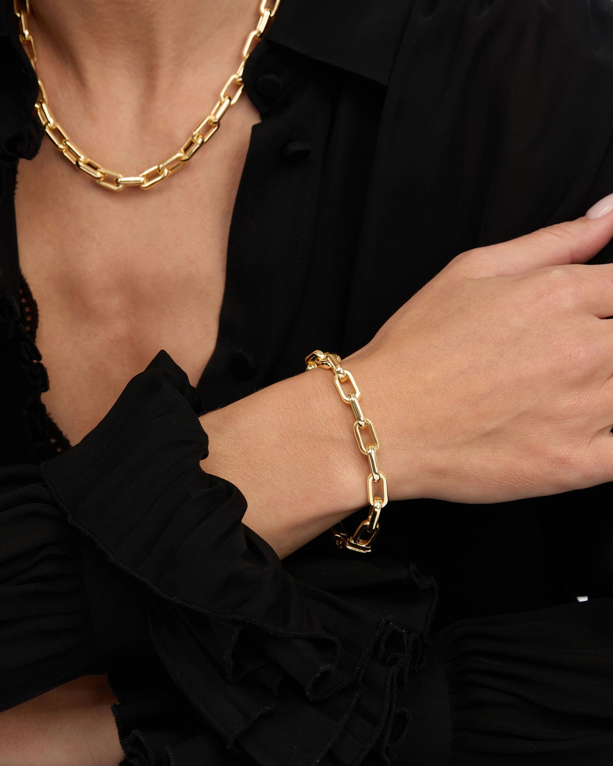Gold chain necklace and bracelet on a person wearing a black outfit