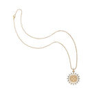 A delicate gold chain necklace with a circular pendant featuring a central gold monogram and a sunburst border accented with small clear stones, shown on a plain white background.