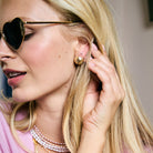 Woman wearing heart-shaped sunglasses and gold earrings, with a neutral background