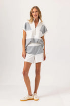 Woman wearing a striped shirt and white shorts on a plain background
