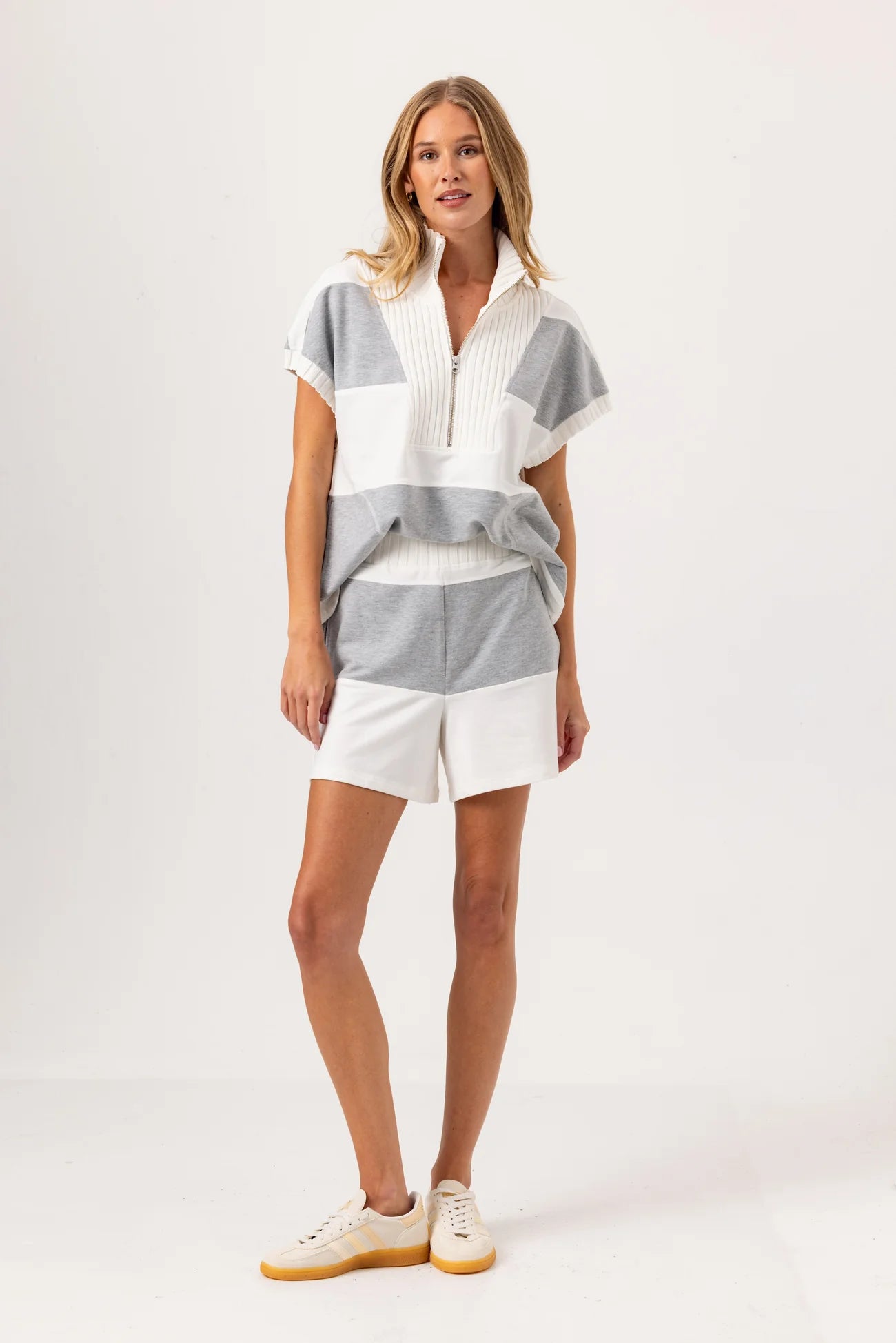 Woman wearing a striped shirt and white shorts on a plain background