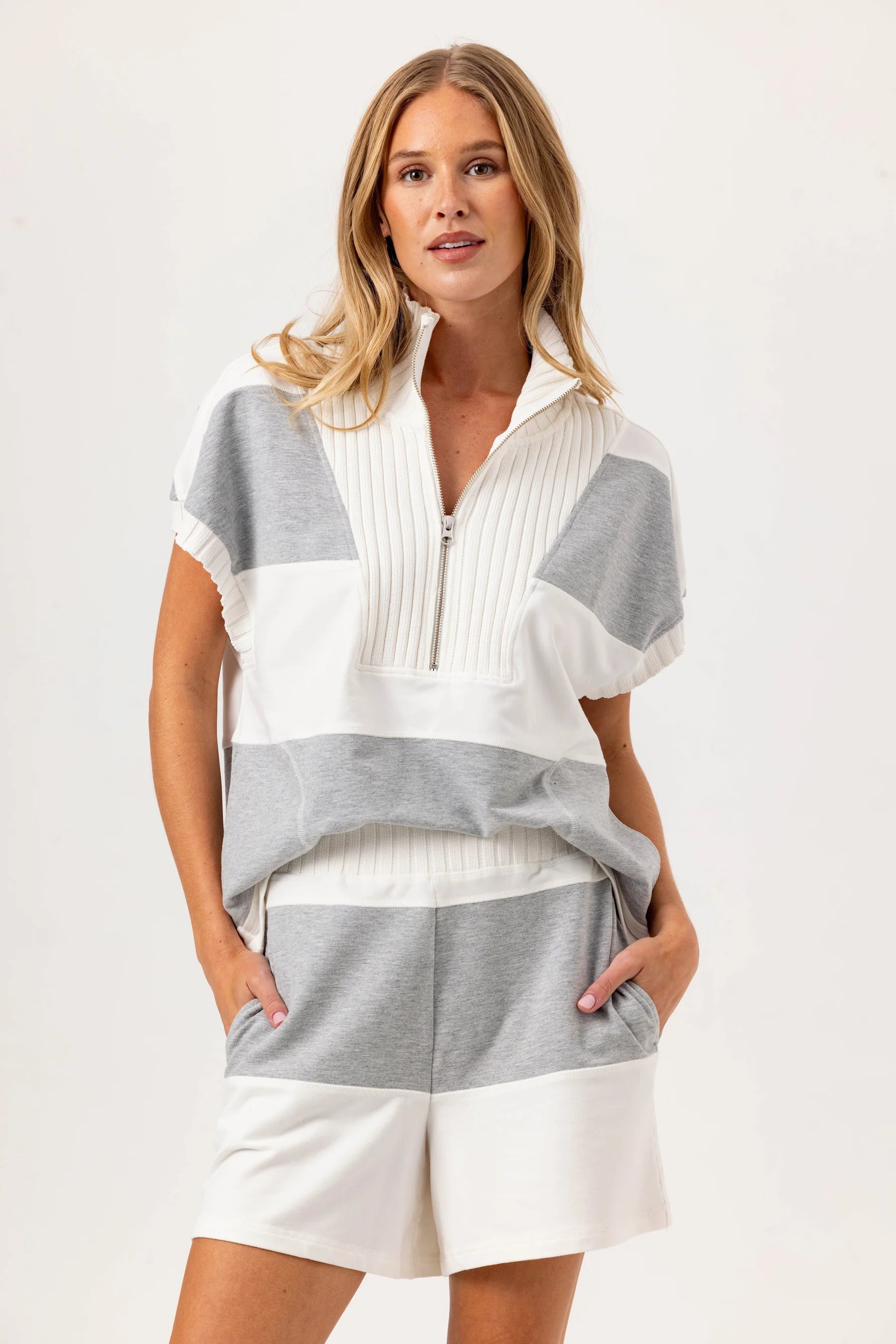 Woman wearing a gray and white striped shirt with a white skirt on a light background