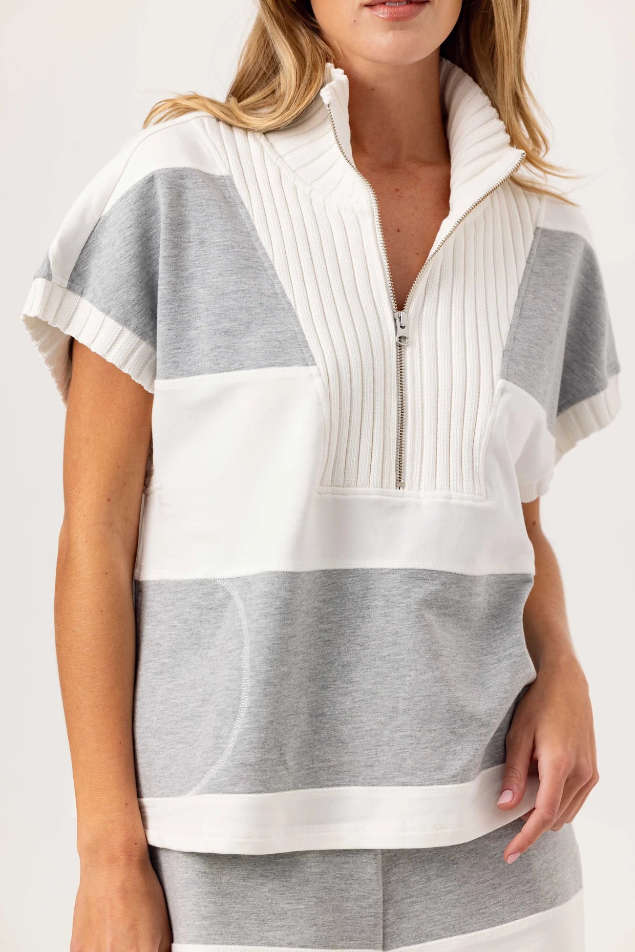 Woman wearing a white and gray striped top with a zipper on a plain background