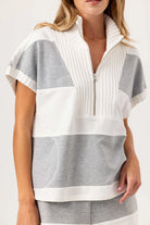 Woman wearing a white and gray striped top with a zipper on a plain background