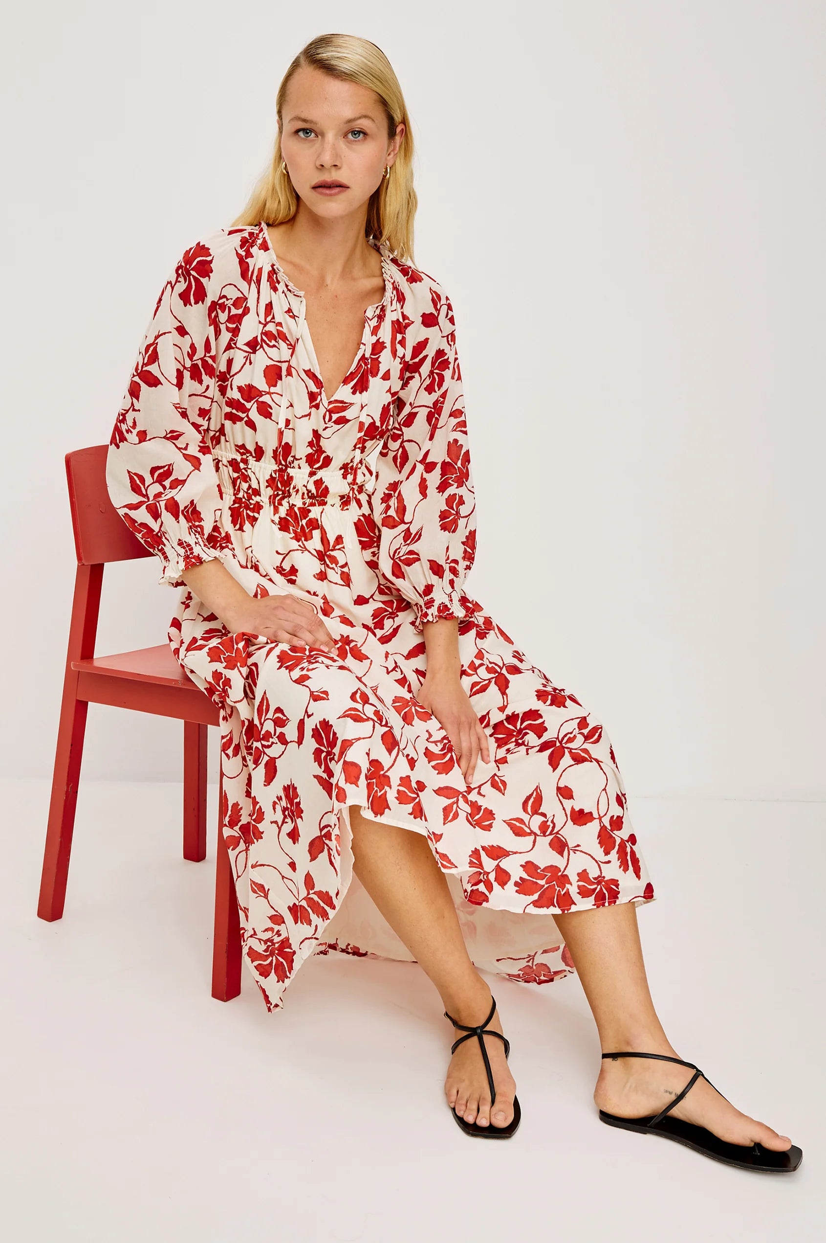 Woman wearing a red floral dress sitting on a red chair against a white background