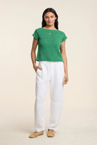 Woman wearing a green top and white pants on a beige background