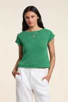Woman wearing a green top and white pants on a beige background