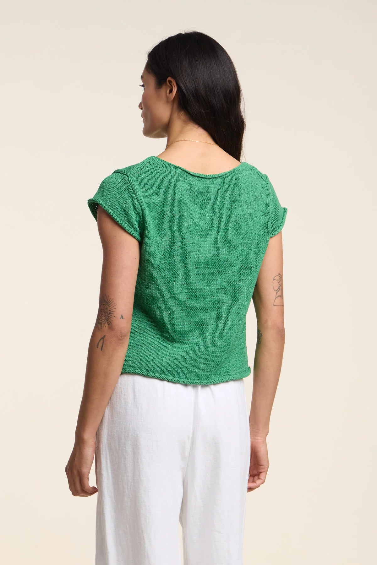 Woman wearing a green top and white pants on a beige background