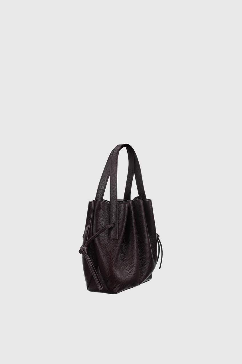 A dark brown leather bucket bag with dual top handles and a drawstring detail, shown against a solid light gray background.