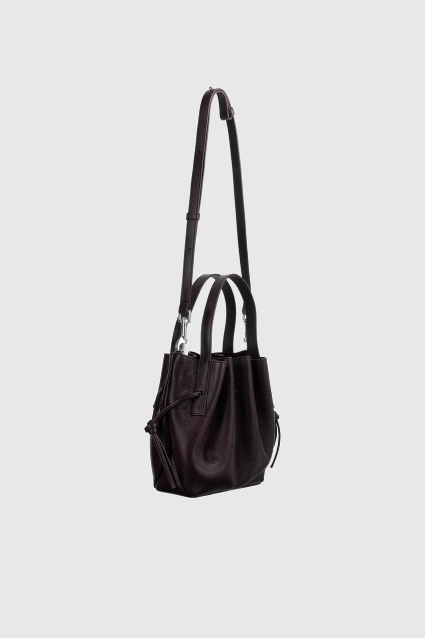A dark brown leather shoulder bag with a long strap, dual top handles, and a drawstring detail, shown against a light gray background.