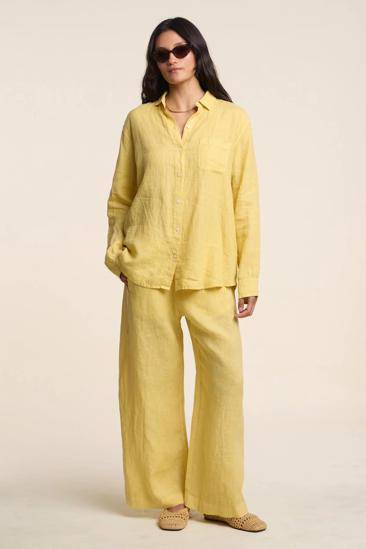 Woman wearing a yellow outfit with sunglasses on a plain background