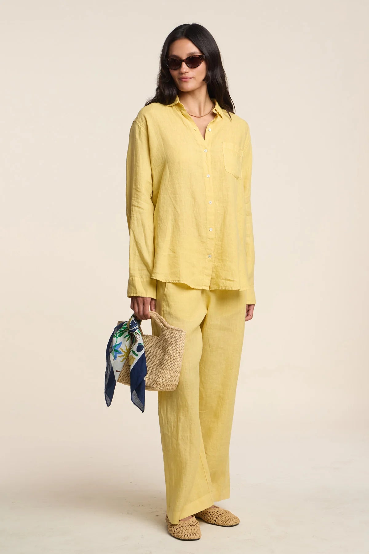 Woman wearing a yellow outfit holding a bag and scarf against a beige background