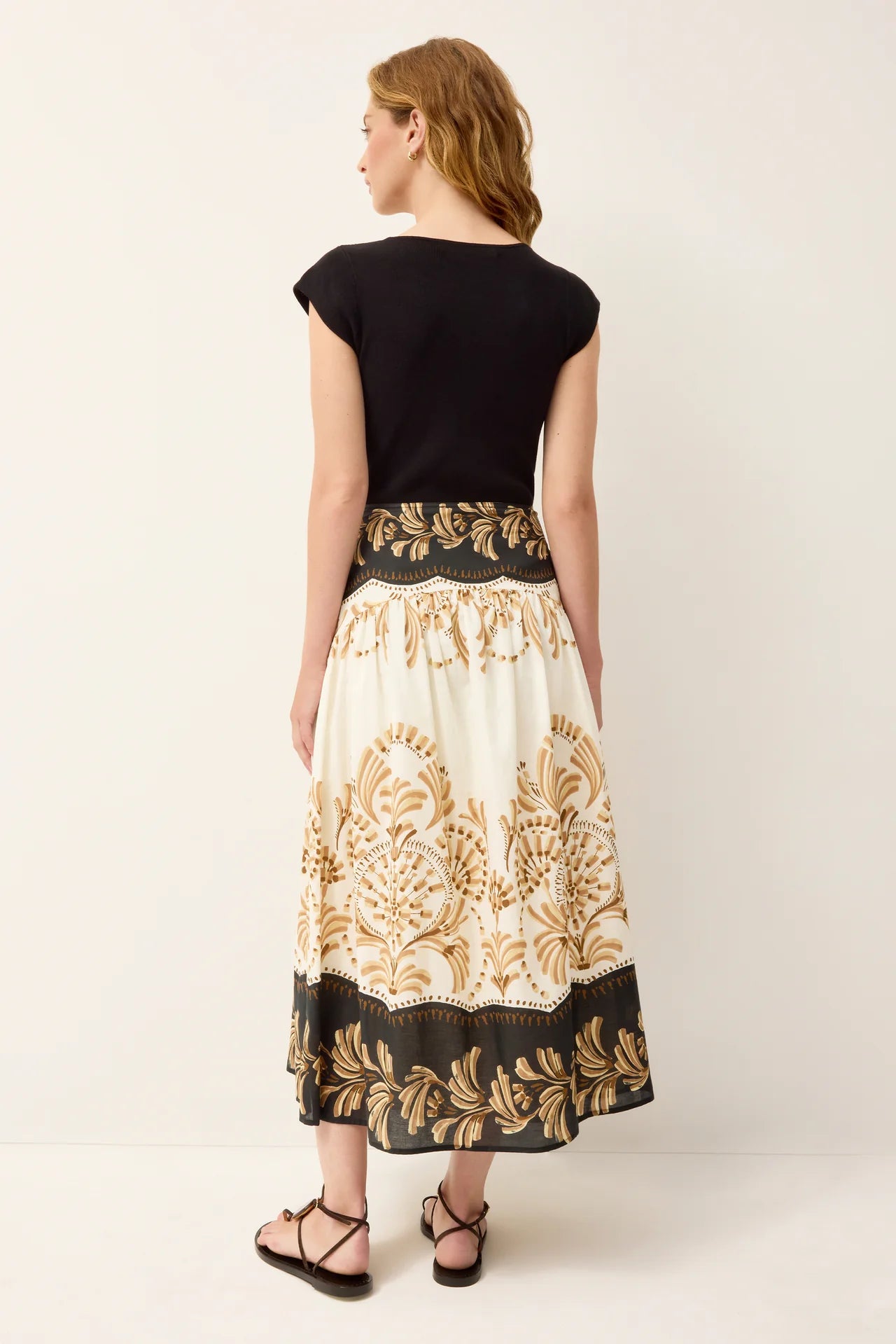 Woman wearing a black top and a long, patterned skirt on a white background