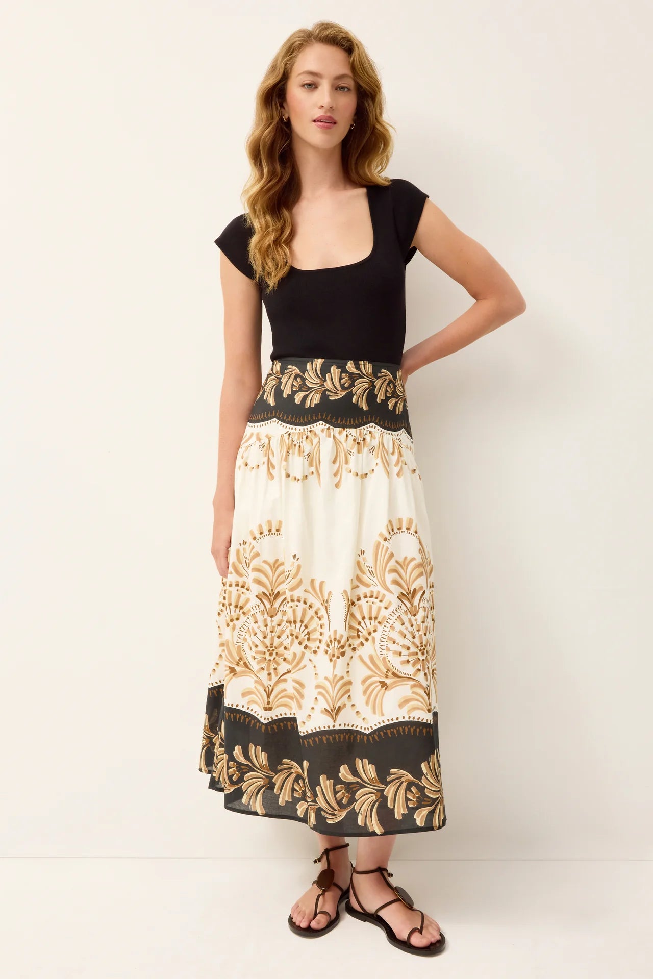 Woman wearing a black top and a long, patterned skirt on a white background
