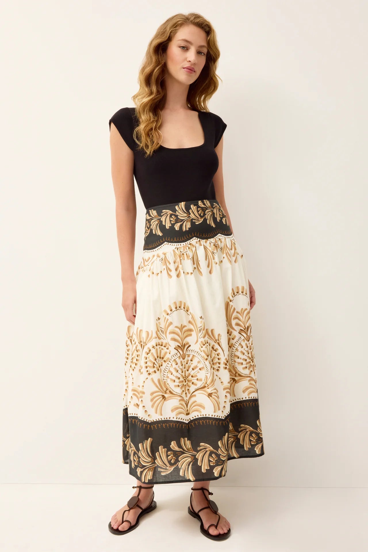 Woman wearing a black top and a long, patterned skirt on a white background