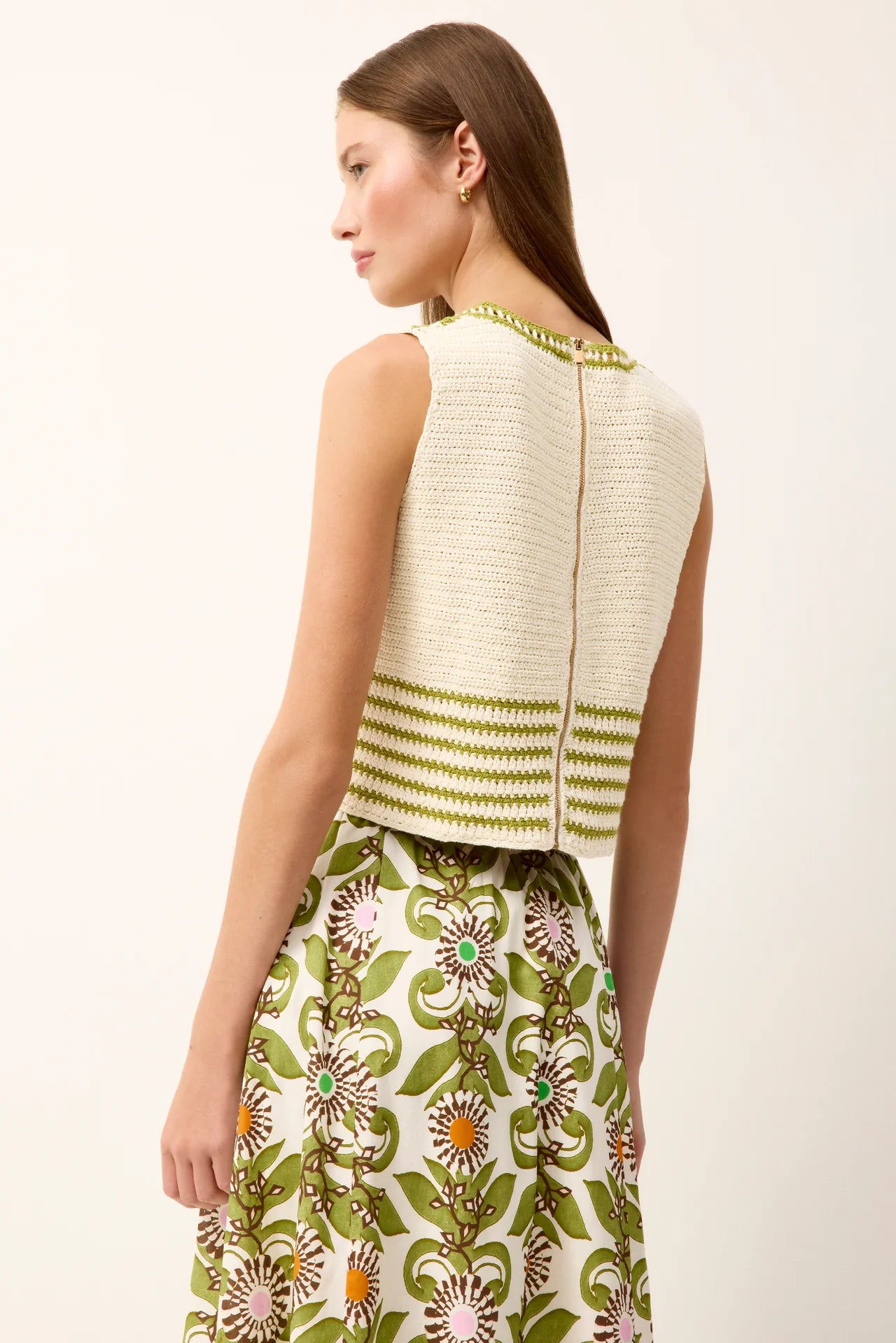 Woman wearing a white sleeveless top with green stripes and a floral skirt on a white background